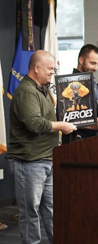 two men standing at a podium with a hero poster in front of them
